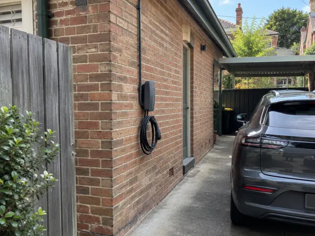 EV charger mounted on a brick exterior wall beside a driveway and parked car in Woollahra