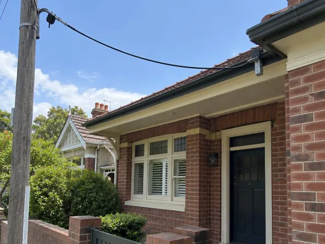 Brick house exterior with overhead service cable and point-of-attachment bracket under the eaves in Bellevue Hill